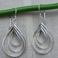 Silver teardrop earrings hanging on a green rod against a gray background
