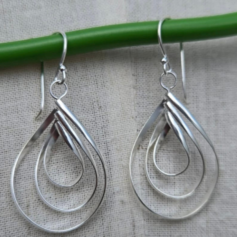 Silver teardrop earrings hanging on a green rod against a gray background