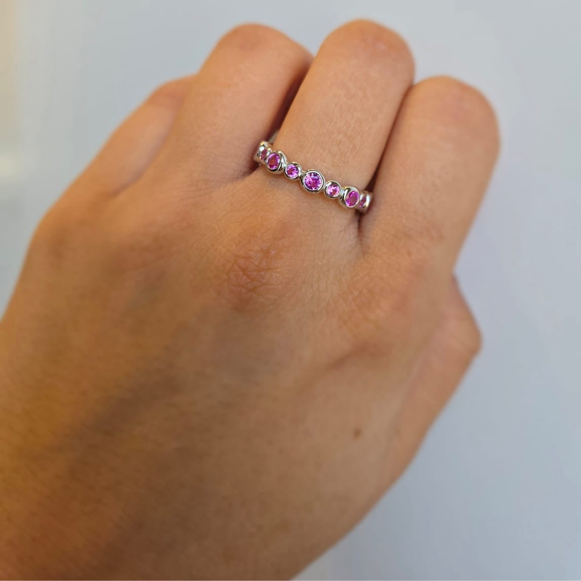 A sterling silver stacking ring with pink cubic zirconia stones worn on a person's hand.