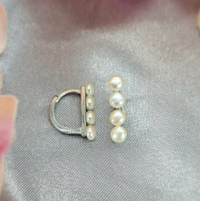 A pair of D-shaped huggy earrings with freshwater pearls on a silver hook, placed on a textured surface.