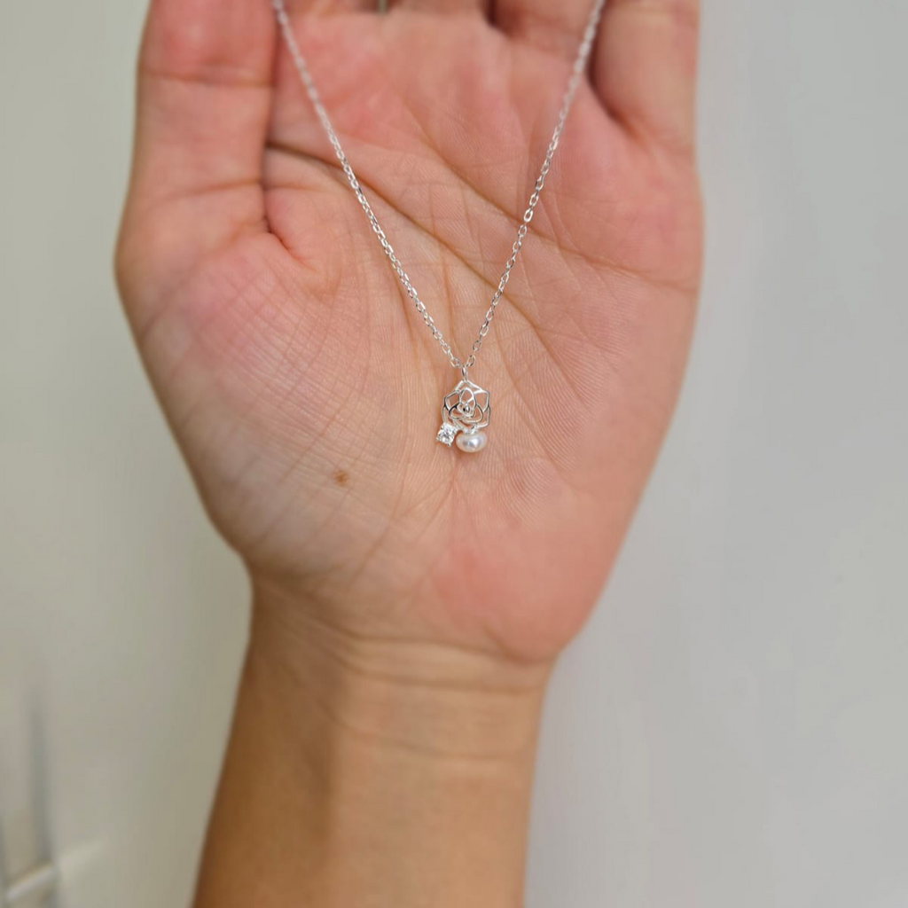 A sterling silver necklace with a rose and pearl pendant, held in a hand against a white background.