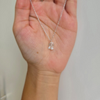 A sterling silver necklace with a rose and pearl pendant, held in a hand against a white background.