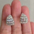 Teardrop-shaped diamond earrings held between two fingers against a neutral background