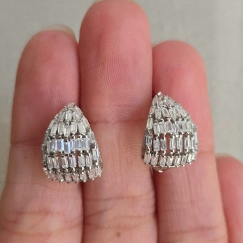 Teardrop-shaped diamond earrings held between two fingers against a neutral background
