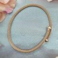 A rose gold plated sterling silver mesh fold over bracelet displayed on a grey surface with flowers in the background.