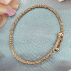 A rose gold plated sterling silver mesh fold over bracelet displayed on a grey surface with flowers in the background.