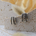 Silver earrings on a textured stone surface with a blurred floral background