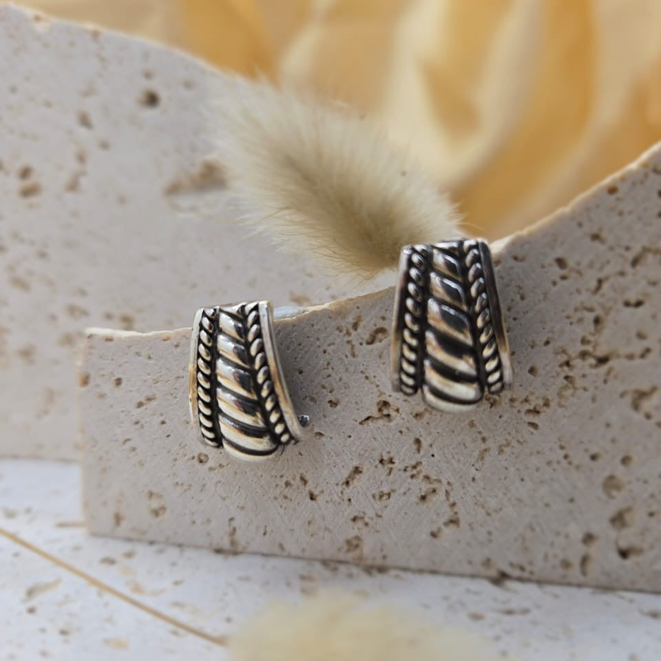 Silver earrings on a textured stone surface with a blurred floral background