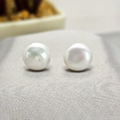 A pair of sterling silver stud earrings with lustrous pearl embellishments, displayed on a textured surface.