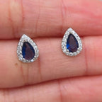 Teardrop-shaped blue gemstone earrings on a hand