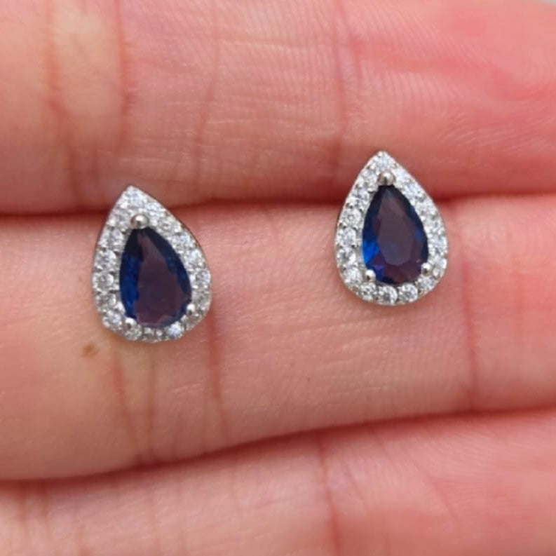Teardrop-shaped blue gemstone earrings on a hand