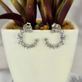 A pair of sterling silver round pavé stud earrings with cubic zirconia embellishments, displayed in a white vase with a green plant.