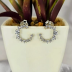 A pair of sterling silver round pavé stud earrings with cubic zirconia embellishments, displayed in a white vase with a green plant.