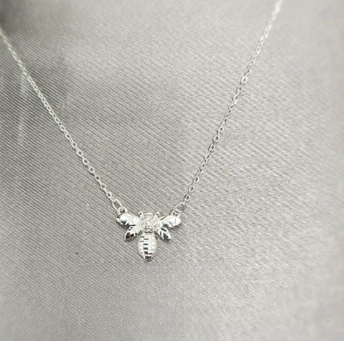 A sterling silver bee necklace with cubic zirconia accents, displayed on a mannequin.