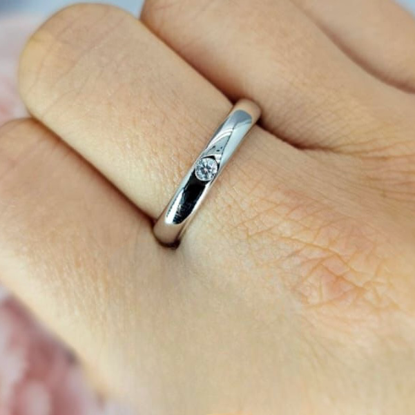 A sterling silver ring with a single cubic zirconia embedded in the band, displayed on a person's finger.