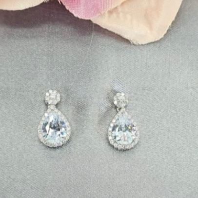 Teardrop-shaped earrings on a gray surface with a pink flower in the background