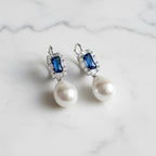 Pearl earrings with blue gemstones on a light gray background