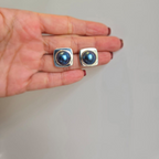 A pair of blue mabe pearl earrings displayed on a person's hand.