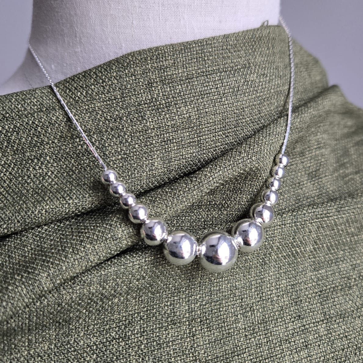 Silver necklace on a mannequin with a green fabric background