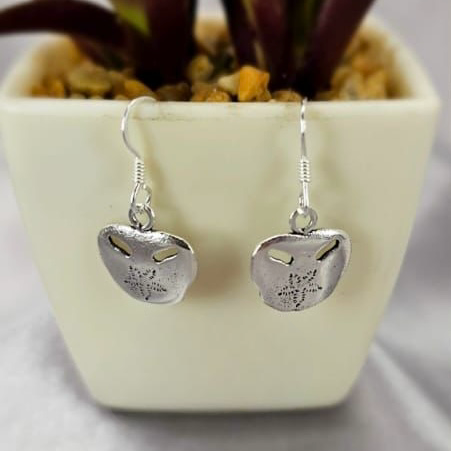 A pair of sterling silver drop earrings with a floral design, displayed in front of a potted plant.