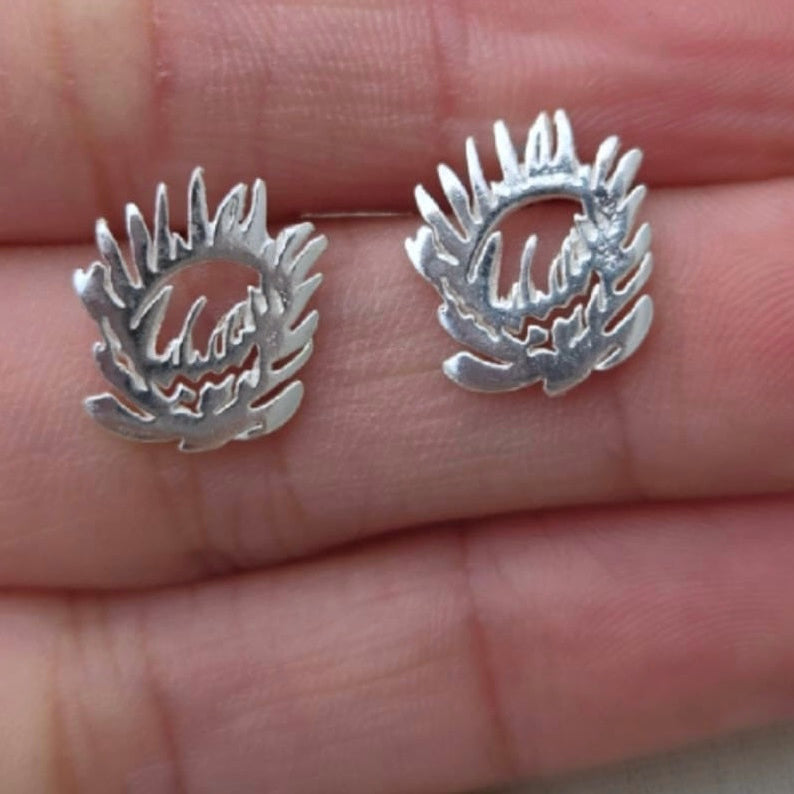 Silver earrings with a wreath design held between fingers on a light skin background