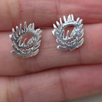 Silver earrings with a wreath design held between fingers on a light skin background