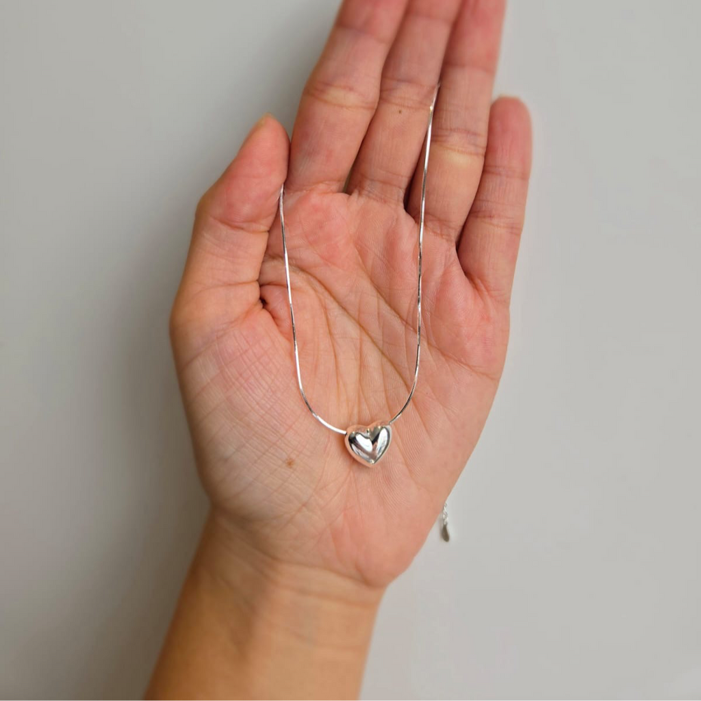 A sterling silver floating heart necklace displayed on a hand.