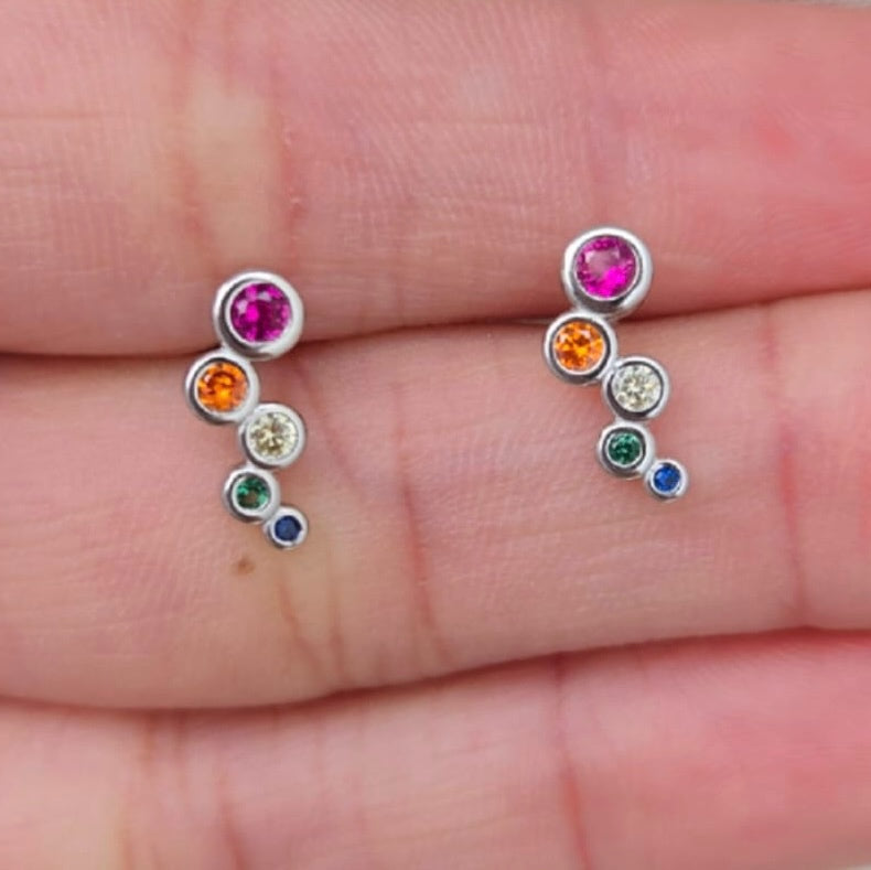 Pair of silver earrings with colorful gemstones held between fingers.