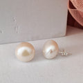 Pearl earrings on a light gray surface with a soft pink fabric background