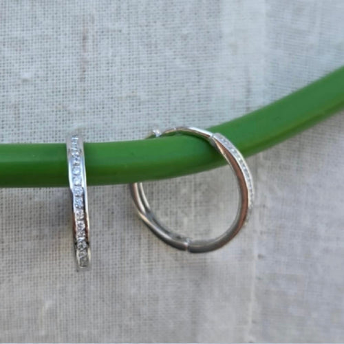 Silver hoop earrings on a green stick against a gray background