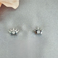 A pair of sterling silver crown stud earrings with a single cubic zirconia centre, displayed on a textured surface.