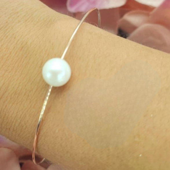 A rose gold plated bracelet with a freshwater pearl on a person's wrist, with a background of pink flower petals.