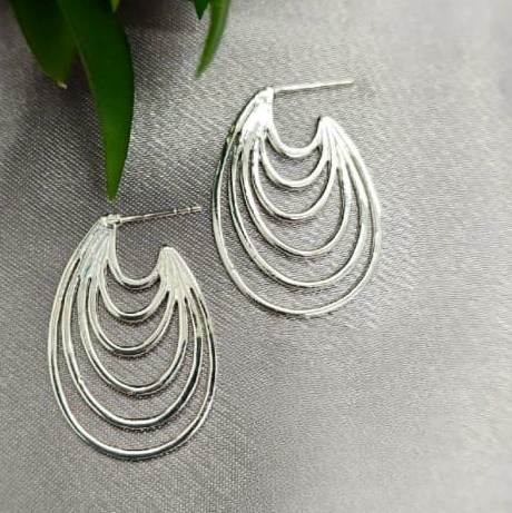 A pair of sterling silver hoop earrings with a six layered design, displayed on a textured surface.