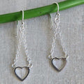 Silver heart-shaped earrings hanging from a green rod on a textured gray background
