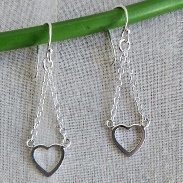 Silver heart-shaped earrings hanging from a green rod on a textured gray background