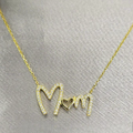 A gold-plated sterling silver necklace with the inscription 'Mom' and cubic zirconia details on a grey background.