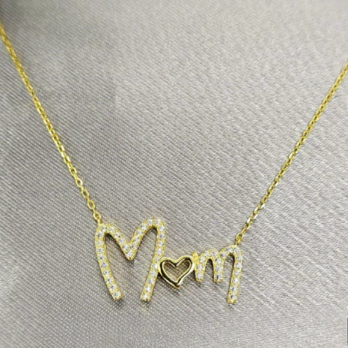 A gold-plated sterling silver necklace with the inscription 'Mom' and cubic zirconia details on a grey background.