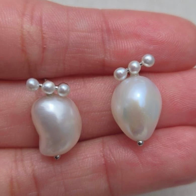 Pearl earrings held between fingers on a light skin background