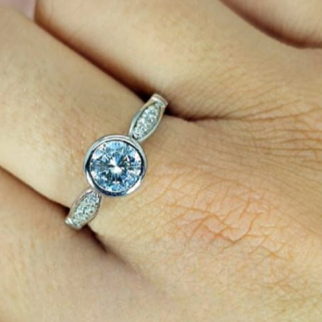 A close-up image of a hand wearing a silver ring with a central cubic zirconia stone and smaller stones on the band.
