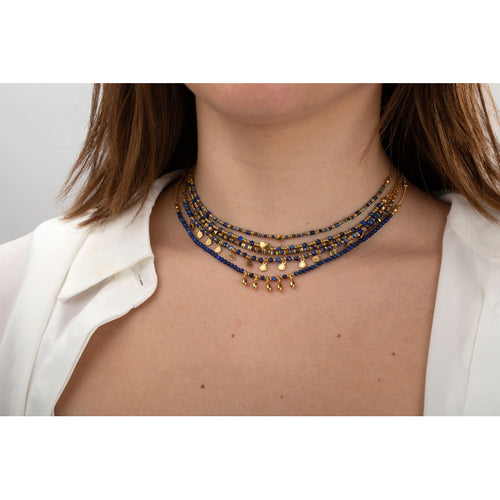 Necklace with blue and gold beads worn by a person against a neutral background