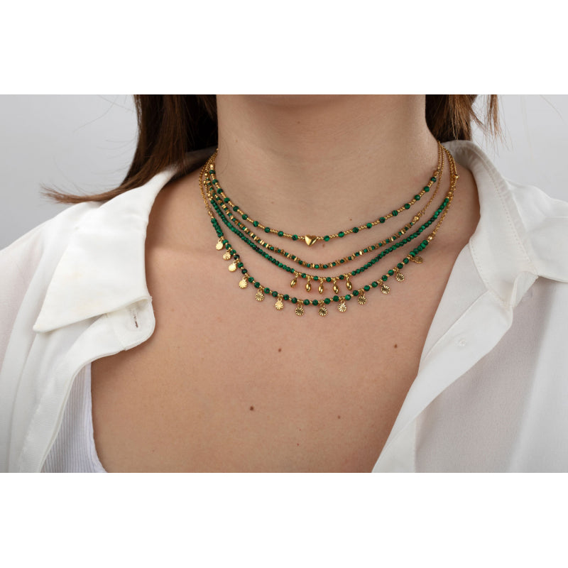 Stack of green and gold necklaces on a person wearing a white shirt.