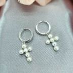 A pair of silver huggy earrings with freshwater pearl crosses on a grey fabric background with a floral accent.