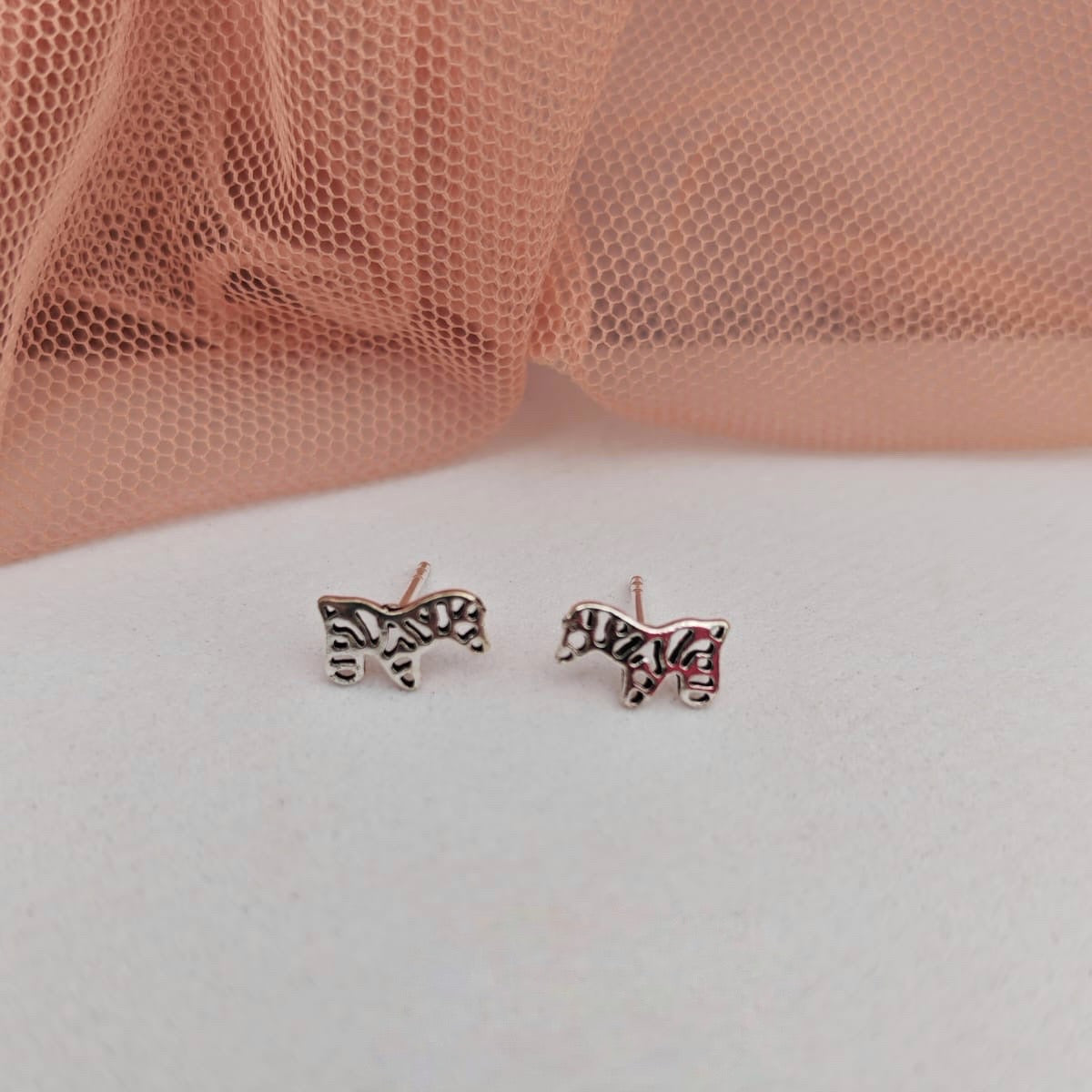 Zebra print earrings on a white surface with a pink mesh background