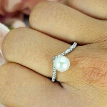 A Sterling silver wishbone ring with cubic zirconia pavé detail and a freshwater Pearl centre, worn on a person's hand.