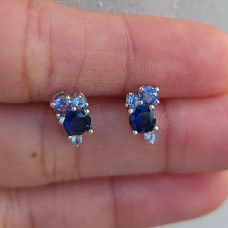 Pair of blue gemstone earrings held between fingers against a neutral background