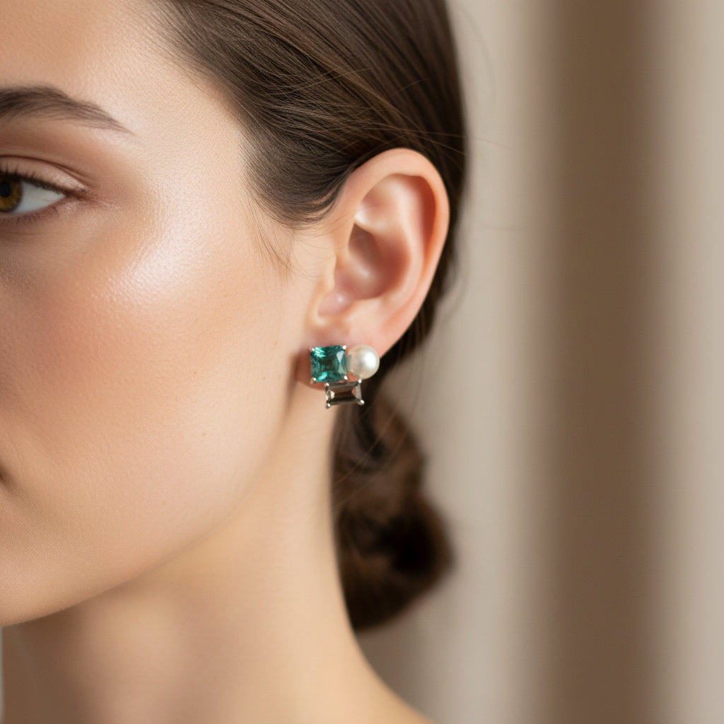 Pair of earrings with green gemstones and pearls on a light surface.