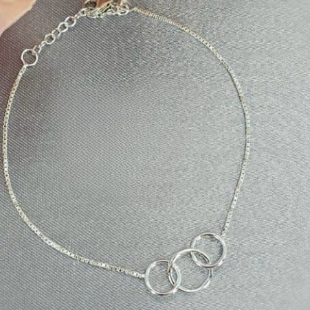 A sterling silver bracelet with three interlinked rings, displayed on a surface with a background of soft focus flowers.