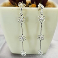 Three tiny silver daisy drop earrings displayed on a plant stem in a white vase.