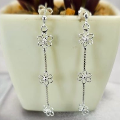 Three tiny silver daisy drop earrings displayed on a plant stem in a white vase.