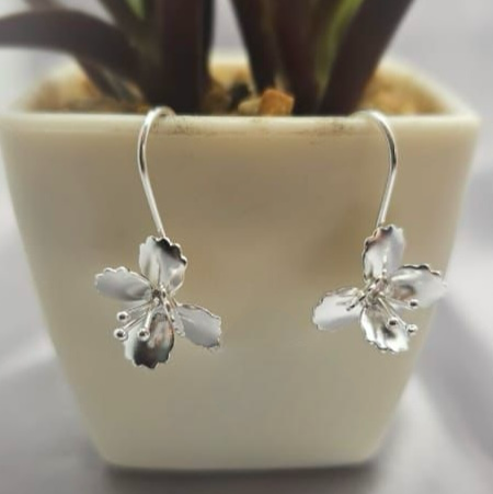 Silver flower-shaped drop earrings displayed in a white vase with a green plant background.